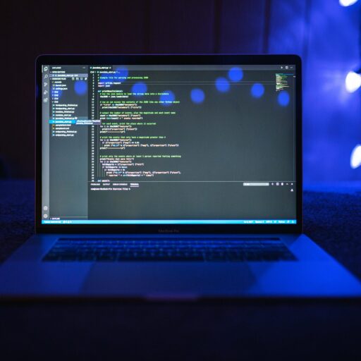 Close-up of a laptop screen displaying code, set against a dark backdrop with blue lighting for a tech-focused ambiance.